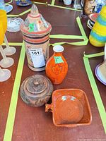 Group view of all four items: painted lidded jar, orange vase, carved wooden pot, orange glazed dish