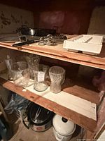 Shelved items: enamel roasting pan, grill rack, metal skewers, generic glass vases, slow cooker partially visible