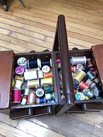Open cantilever sewing box showing many thread spools
