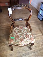 Front view of carved wood chair, showing floral carved crest and upholstered seat