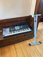 Yamaha YPT-220 keyboard on wooden surface, manual on left, metal stand beside