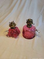 Both cranberry glass oil lamps side by side showing overall form and burners