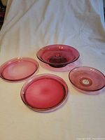 Four cranberry glass pieces arranged on cloth backdrop