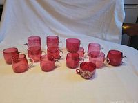 Group of 16 cranberry glass handled cups arranged on white cloth