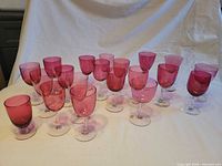 Front view of 20 cranberry glass stemmed wine glasses arranged on table