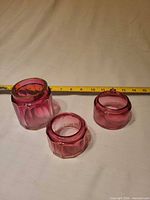 Three pink faceted glass dresser jars without lids shown alongside measuring tape for scale