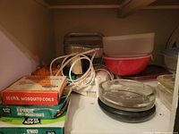 Shelf with mosquito coil boxes, aluminum pans, hand mixer, mixing bowls, ashtray