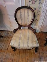 Front view of Victorian chair showing oval back, wood frame, striped floral upholstery, casters