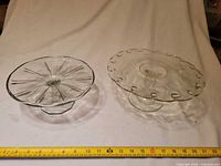 Both pressed glass cake stands side by side with tape measure for scale