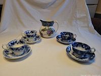 Group shot: four flow blue cups on saucers with Losol Ware jug centred