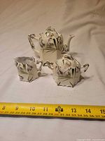 Front view of teapot, sugar bowl with lid, and creamer with tape measure for scale