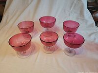 Six cranberry glass compotes displayed on cloth