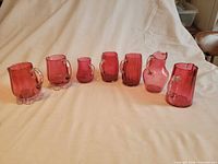 Seven cranberry glass creamers lined up