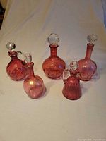 Front view of five cranberry glass decanters showing shapes and stoppers