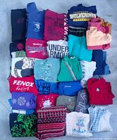 Top-down view of folded sweaters and vests grid showing variety of colors, graphics and logos