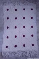Full view of white crochet blanket with floral motifs and fringe