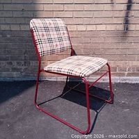 Side view of red metal stacking chair with Burberry plaid upholstery against brick wall