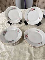 Group view of all eleven floral dessert plates, two displayed on stands, remainder stacked