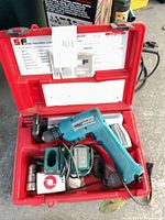 Open red case showing Makita drill, charger, battery, metal fastener parts and instruction panel