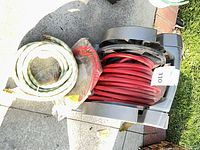 Overall lot showing green-white garden hose, separate red hose in plastic, and grey hose reel with coiled red hose
