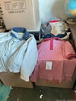 Overview showing light beige windbreaker and Prince Club top on boxes with additional folded tops