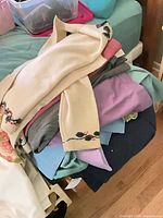 Pile of folded sweaters and tops with cream embroidered sweater on top