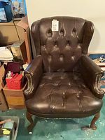 Front view of brown wingback tufted armchair showing seat, back, arms, nailhead trim, cabriole legs