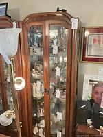 Full view of curio cabinet showing brown wood frame, double glass doors, interior collectibles for scale