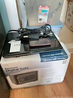 Stack showing HP laptop, LG phone, charger atop boxed Bunker Hill safe