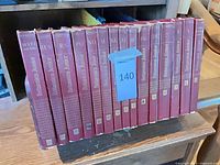 Row of 15 red Encyclopaedia Britannica Junior hardcover volumes on shelf, volume numbers visible