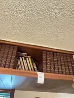 Upper shelf showing two groups of brown Encyclopedia Britannica volumes and assorted smaller books