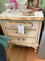 Front view of cream and gold French Provincial nightstand showing three drawers and hardware