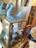 Tabletop glass/brass cabinet filled with figurines, blue swan on top