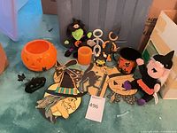All items grouped: bowl, plush witches, candle, mug, metal silhouette, headband, wooden cutouts