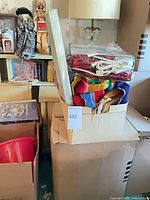 Box containing several packaged textiles including blinds box, serape blanket, heated throw