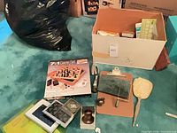 Lot overview showing boxed 7-in-1 game, clipboard, stapler, frames, paddle in open box