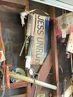 Pneumatic grease gun, lever grease gun, black bulk grease gun, and pressure gauge visible hanging on wall