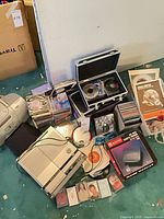 Group shot of both boomboxes, CDs, cassettes, VHS rewinder box, storage case and manuals