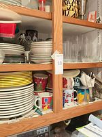 Cupboard shelf with stacks of dinner plates, mugs and tumblers