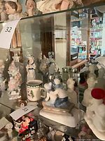Shelf view showing multiple porcelain figurines, sled scene, mug, Mickey Mouse, and additional small figures