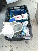 Crate containing white outdoor light fixture, herbicide box, blue bin, gloves, towels