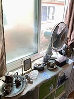 Overview showing desk fan, silver tea set on lace runner, clock, glass box, radio, figurines