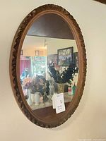 Full view of oval mirror mounted on wall showing carved wooden frame