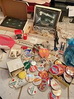 Lot overview showing buttons, keychains, lapel pins, visor, name badge and pin display box