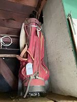 Full view of red nylon golf bag standing upright showing strap, pockets and base