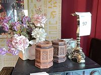 Group shot showing artificial flowers, two carved holders, metal candlestick, glass votive