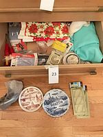 Drawer with textiles, packaged gadgets; two souvenir plates and four ice cube trays in front