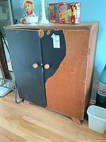 Front view of cabinet with natural wood and black doors showing wear and peeling veneer