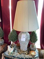 Lamp with shade flanked by two topiaries, hen figurine and amber bowl visible on tabletop
