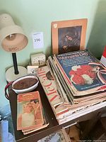 Overall view of lot on table showing magazines, books, lamp, dish, clocks, plaque
